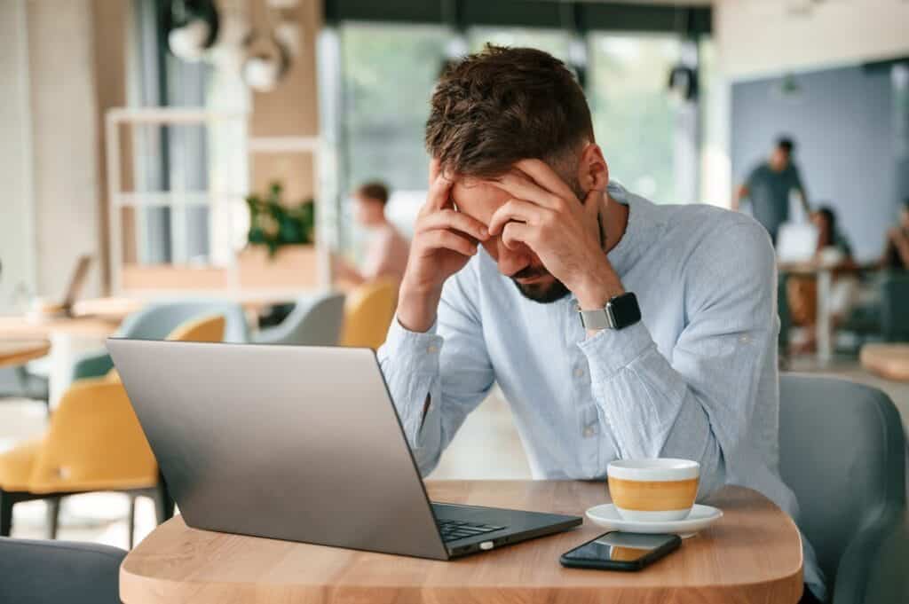 Fear of Abandonment Will Gaslight Your Brain Into Ruining Relationships as depicted in this image of a Young man is sitting alone in the cafe and working by using laptop.