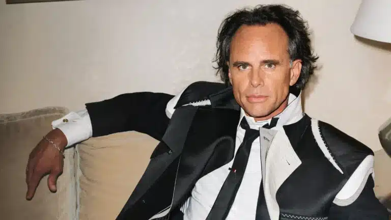 Walton Goggins lounges in a tailored, patchwork black-and-white suit, staring directly at the camera with a stern, unreadable expression, evoking the charismatic yet emotionally distant persona often attributed to avoidant attachment styles.