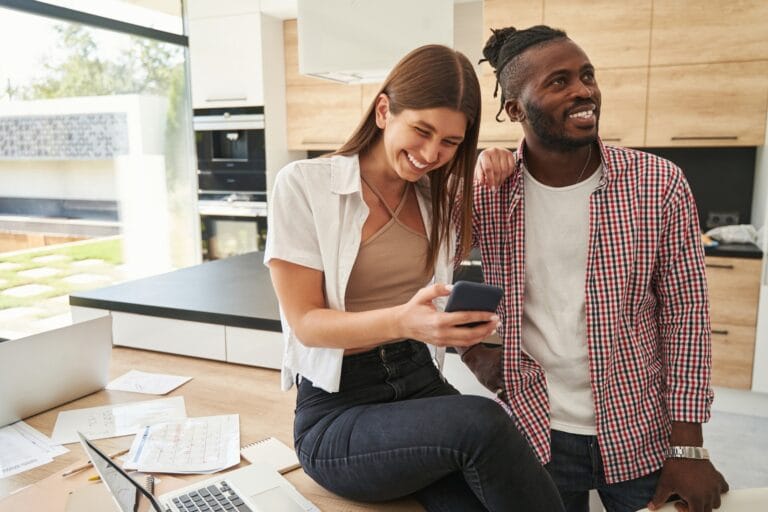 Joyous lady with gadget and pleased guy in kitchen