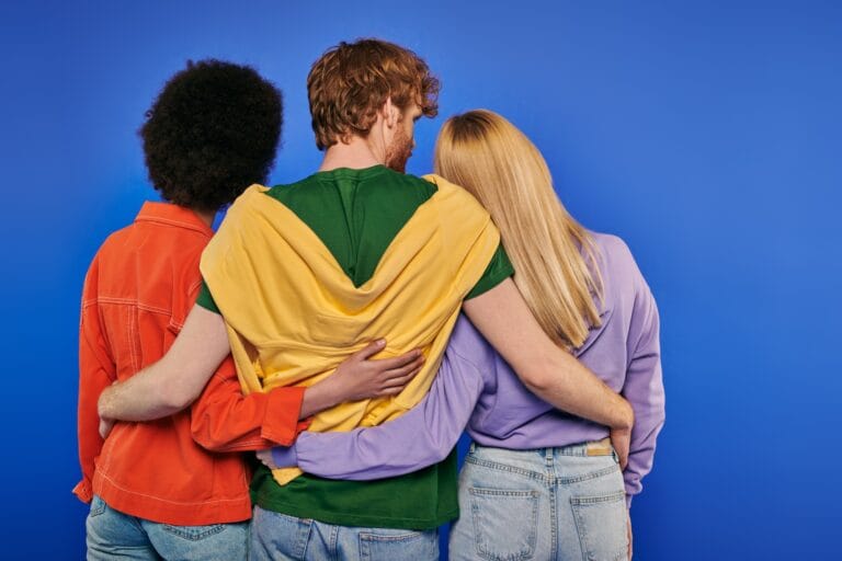 love triangle, polyamory lovers, back view of young redhead man hugging multiracial women on blue