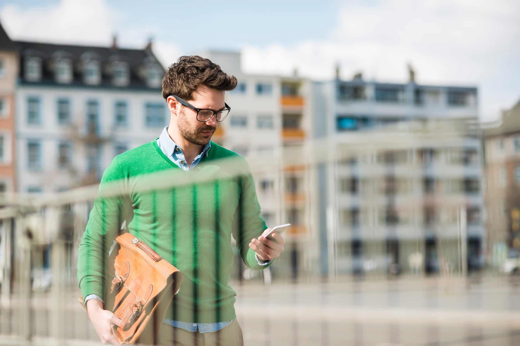 Man in green sweater carrying briefcase, reading text message