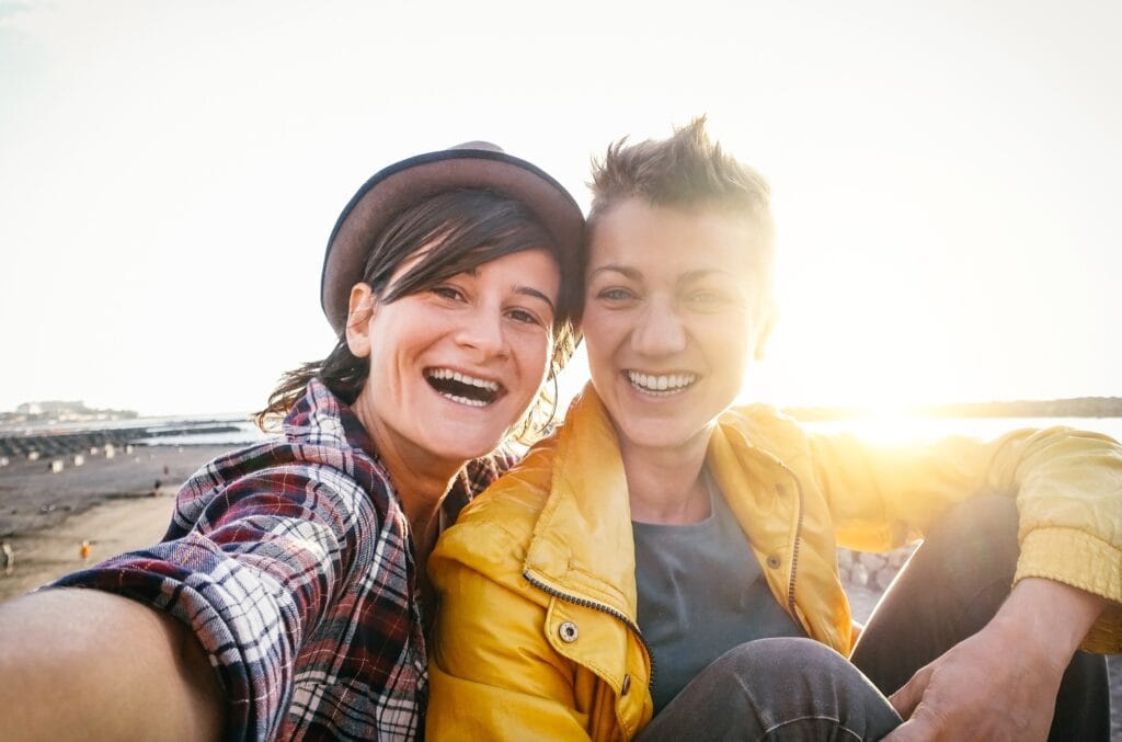 Happy gay couple taking selfie on the beach at sunset - Young lesbians having fun dating first time