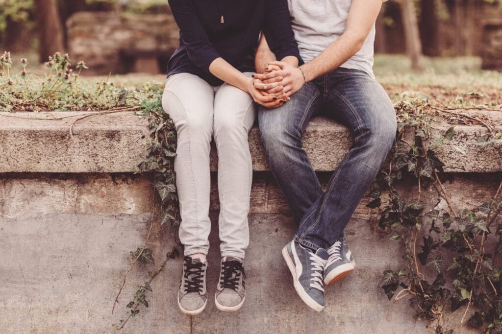 Two people sitting close together on a stone ledge, holding hands tightly, symbolizing one of the 5 signs your fearful avoidant ex actually wants you back.