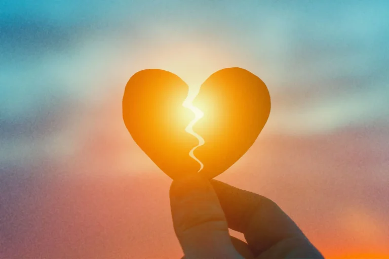 A hand holding a broken paper heart against a glowing sunset, symbolizing the pain of when someone runs away from a good relationship.