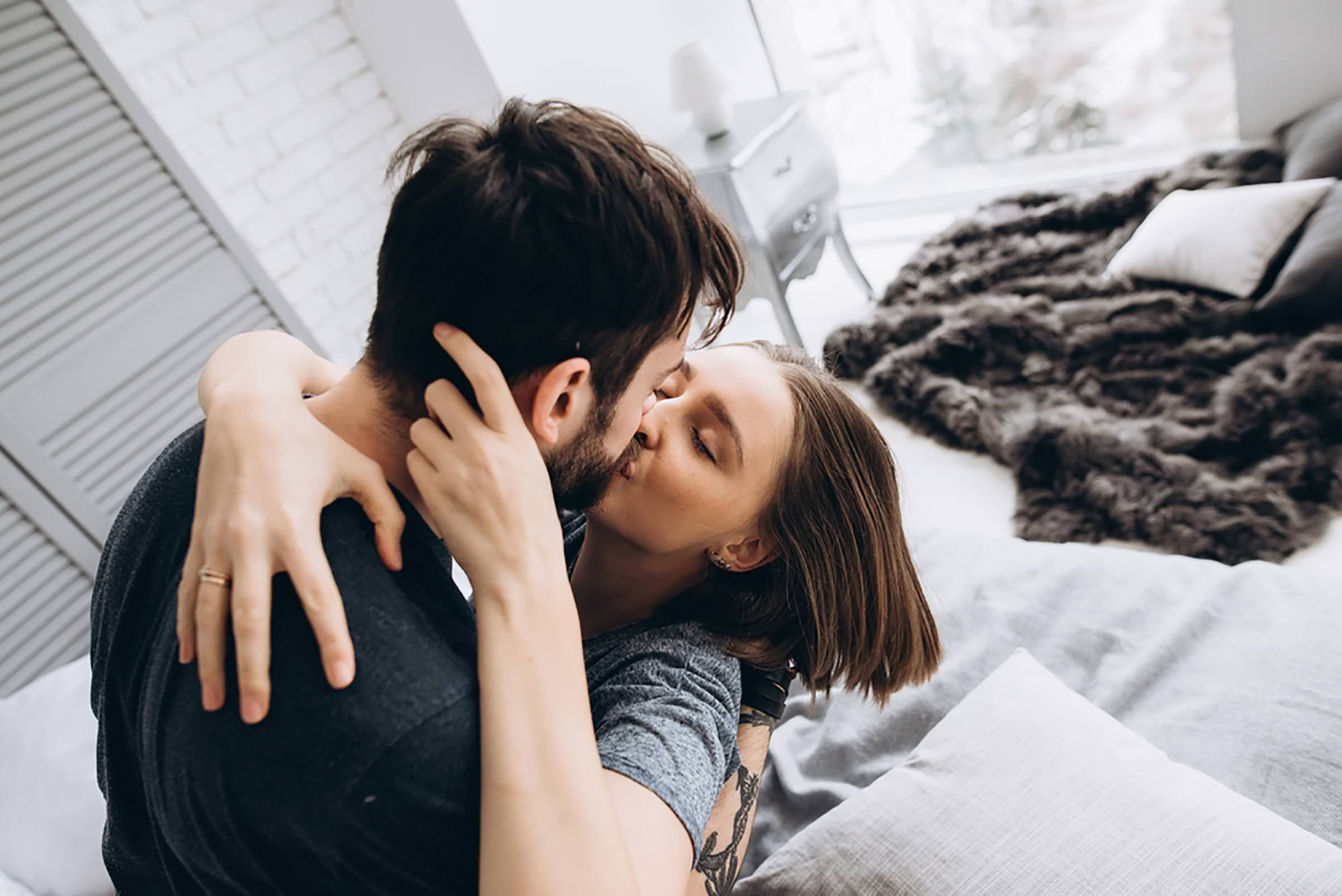 A woman embraces and kisses her partner on the bed, showing physical closeness that often follows when a fearful avoidant ex returns.