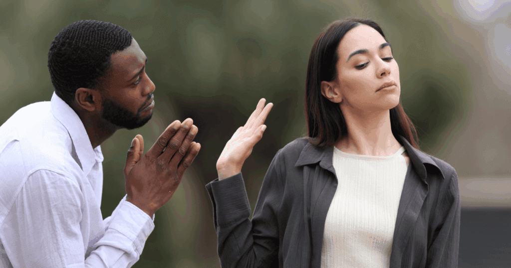 A man pleads while a woman looks away and raises her hand to dismiss him, symbolizing emotional distancing seen in fearful avoidant women.